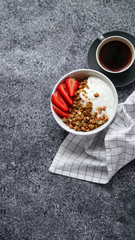 Perfect breakfast: crunchy granola with yoghurt and strawberries with a cup of black coffee on gray bakcground. Flat lay with copy space