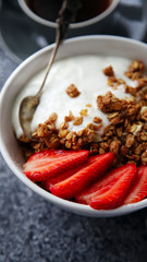 Close up shot of perfect breakfast: crunchy granola with yoghurt and strawberries with a cup of black coffee on gray bakcground.