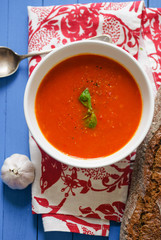 Tomato soup garnished with basil leaves served with rye bread on blue wooden table