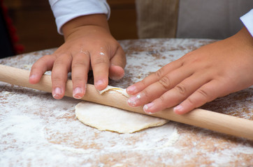 Child hands rolling dough with rolling pin on wooden table