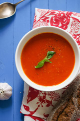 Tomato soup garnished with basil leaves served with rye bread on blue wooden table