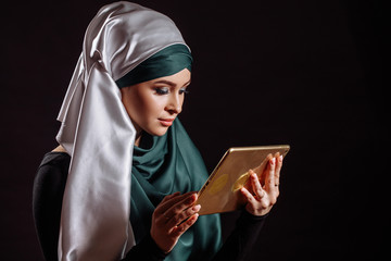 close up portrait of fashion Muslim female looking at the screen of tablet isolated black background. muslim blogger