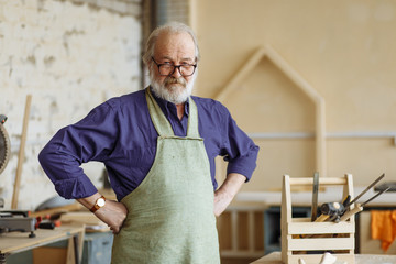 Confident and successful old grey haired man with hands on the hips at workplace