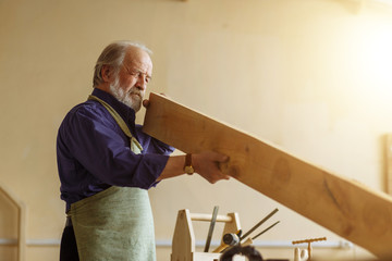 old handsome joiner is measuring the board in the workroom.craftsmanship concept