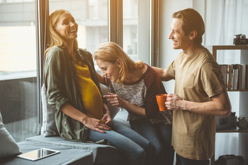 Excited married couple is speaking with unborn child in female abdomen. Pregnant woman is sitting...