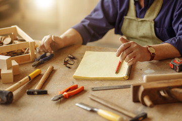 close up cropped photo of craftsman sitting on the wooden desk with various instruments for...