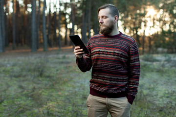 Portrait of adult man walking in the pine forest with digital tablet.