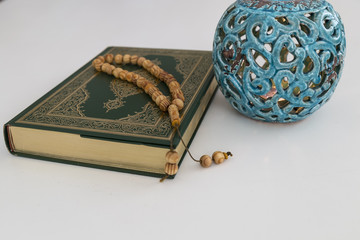 Koran and rosary on the white background with blue candle for Islamic concept. Holy book Quran for Muslims for Ramadan and three months.