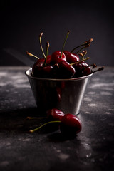 Sweet ripe cherries in metal pail on a table. Beautiful juicy berries on the dark background.