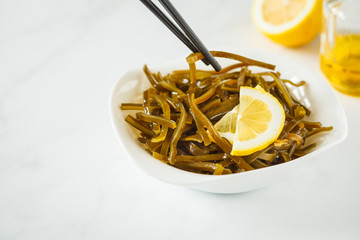Sea kale kelp salad with oil and lemon in a white plate, white background, copy space