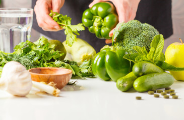 Preparation of green salad. Ingredients for salad on white table. A woman is cooking vegan food.