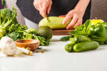 Preparation of green salad. Ingredients for salad on white table. A woman is cooking vegan food.