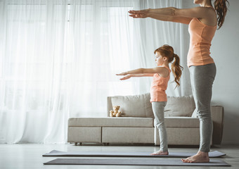 Fototapeta premium Daughter and mom are standing and holding their hands in front of them. Girl looking serious and concentrated. Copy space in left side