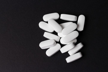 A handful of oval, white tablets lie on a black background.