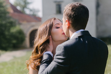 happy wedding couple walking holding hands in evening field on background of old castle. elegant bride and groom embracing. romantic moment. man in suit with bow tie and woman in dress with pearls