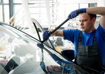 Automobile special workers remove old windscreen or windshield of a car in auto service station...