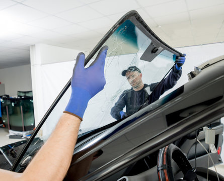 Automobile special workers remove old windscreen or windshield of a car in auto service station garage.