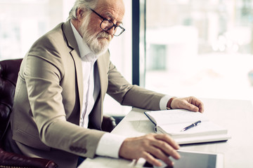 close up side view shot of successful senior chief sitting at work and using the tablet in the office with modern interior.