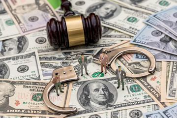 Mini figures with handcuffs and judge's gavel on dollar background