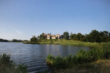 Obraz premium happy wedding couple walking holding hands in evening field on background of old castle. elegant bride and groom embracing. romantic moment. man in suit with bow tie and woman in dress with pearls
