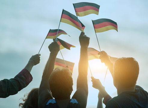 German flags gathering. Raising small deutsch flags to the blue sky, back view.