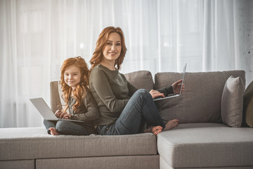 Full length portrait of cheerful mother and daughter with their computer on lap. They are looking...