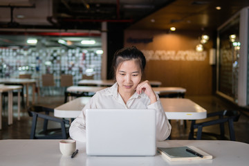 Fototapeta premium Searching for new solution. Pensive young beautiful businesswoman working on laptop and keeping hand on chin while sitting at her working place