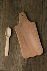 a wooden spoon and a wooden cutting board lie on a wooden table. vertical image