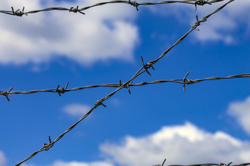 Barbed wire against the blue sky and white clouds