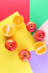 Fruits of oranges and red apples on a multicolored background, halves of oranges and apples on colored paper. Copy space. Citrus in the style of pop art