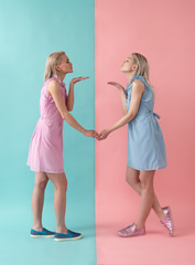 Side view profile of pretty girls in dresses holding hands and sending air kisses one another