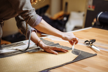 Cropped view female fashion designer marking cloth pattern with chalk on textile materials....