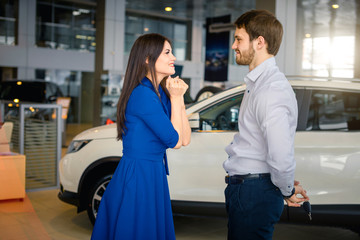 Young emotional woman begging her husband to buy her a new car at dealer office