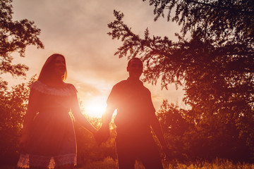 Couple walking in spring forest. Young man and girl holding hands at sunset.