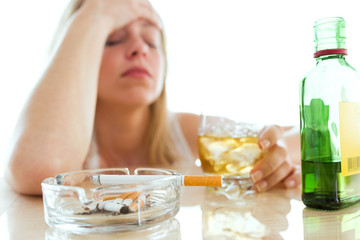 Depressed young woman drinking glass of whiskey and smoking at home.