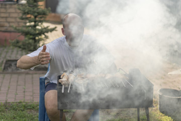 A man with a beard near the fire and the grill fry meat and sausages