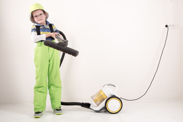 Happy guy in bright green pants and hat removes the dust in house with the help of yellow compact vacuum cleaner.