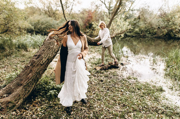 A beautiful couple in the boo style embraces sitting on a branch over the lake