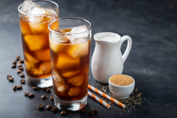 Ice coffee in a tall glass over and coffee beans on a old rustic wooden table. Cold summer drink on a dark background with copy space