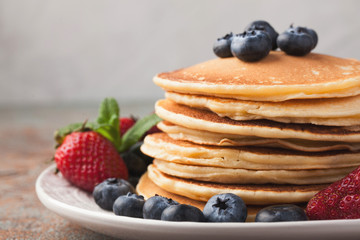 Close-up delicious pancakes, with fresh blueberries, strawberries and maple syrup on a rusty background. With copy space