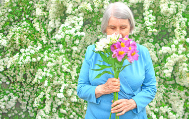 Happy elderly. Elderly woman walks along the street. Beautiful aged woman goes with a bouquet of flowers in garden..