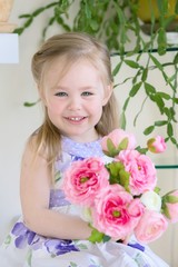 Beautiful little smiling blond girl in dress holds bouquet of Ranunculus