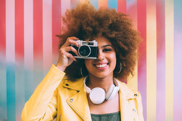 Mixed race woman in a colorful artwork background wall holding a vintage camera