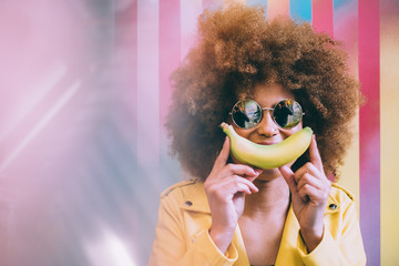 Surprised mixed race woman in a colorful artwork background wall playing with a banana