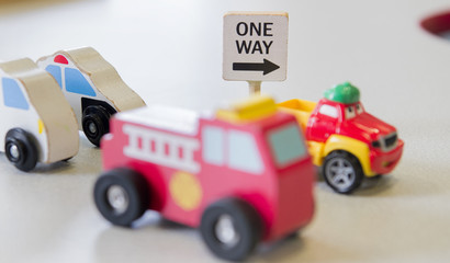 A One Way sign is shown next to a childs toy cars