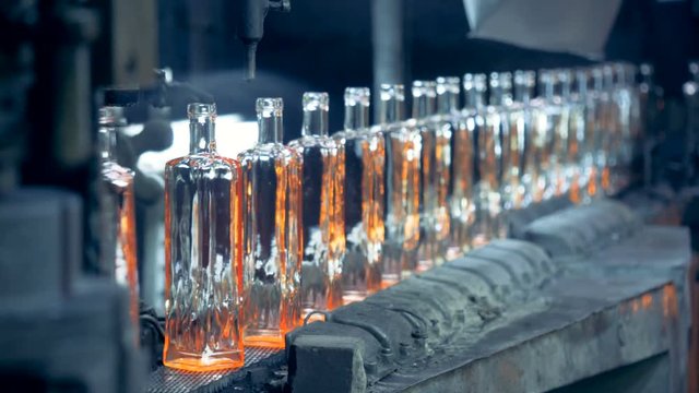 A line of incandescent newly-made glass bottles is moving along the conveyor belt