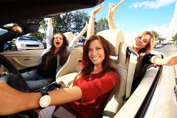 three girls driving in a convertible car and having fun.