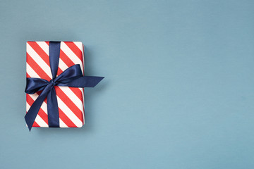 One gift box wrapped in red striped paper and tied with blue bow on blue-gray background. Holiday...