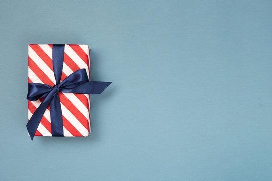 One gift box wrapped in red striped paper and tied with blue bow on blue-gray background. Holiday concept, top view, place for text.