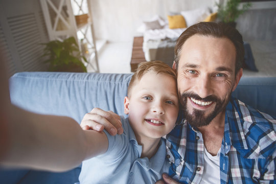 Portrait of cheerful bearded parent and happy child making photo by camera